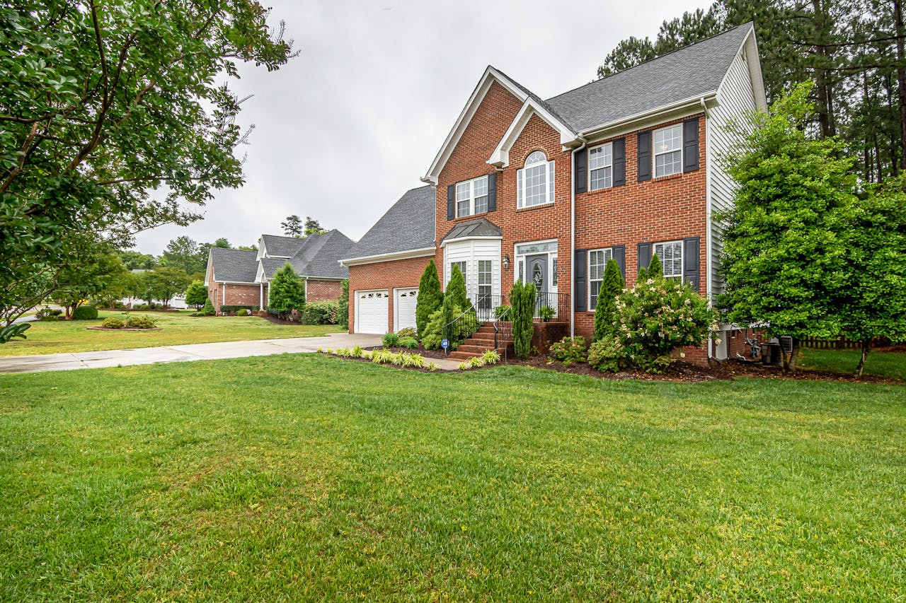 contact-img Charming two-story brick house with manicured lawn and trees, perfect family home.