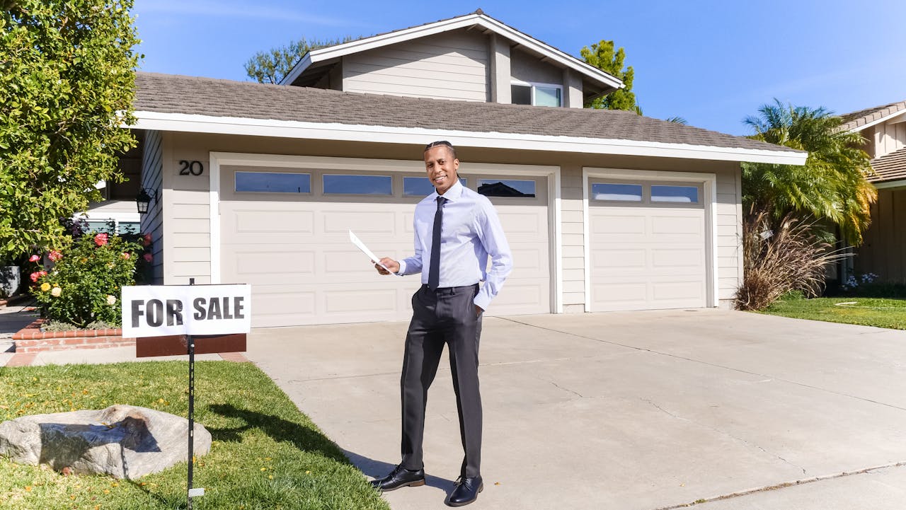 hero-img-02 Real estate agent standing outside a house with a for sale sign in the driveway.