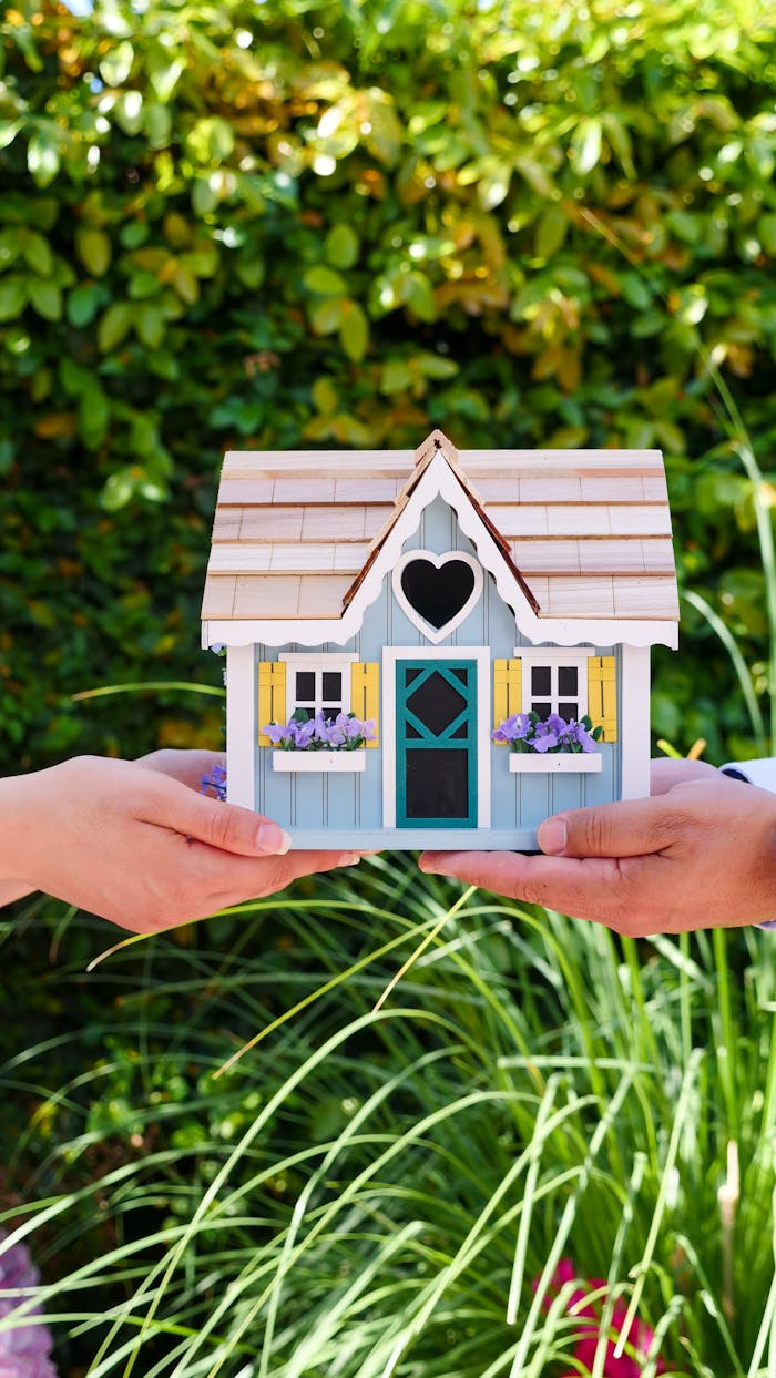gallery-3 Two hands hold a colorful miniature house outdoors, symbolizing real estate and home ownership.