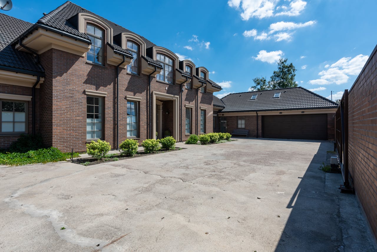about-img Elegant brick house exterior with a large driveway under a clear blue sky.