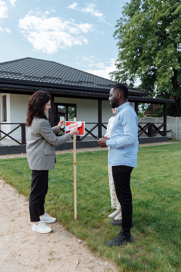 services-01 A couple celebrates buying a new home, placing a sold sign in the yard on a sunny day.